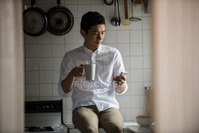 Человек, использующий мобильный телефон во время чашки кофе дома — стоковое фото