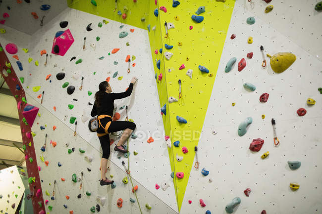 Женщина практикует скалолазание на искусственной стене в спортзале — стоковое фото