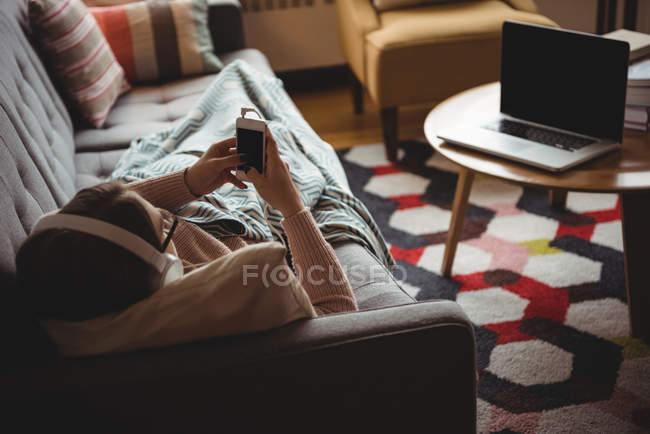 Frau liegt zu Hause auf Sofa und hört Musik mit Handy im Wohnzimmer — Stockfoto