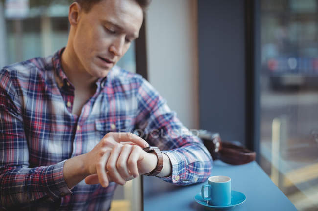 Jovem verificando o tempo em smartwatch enquanto toma café na cafetaria — Fotografia de Stock