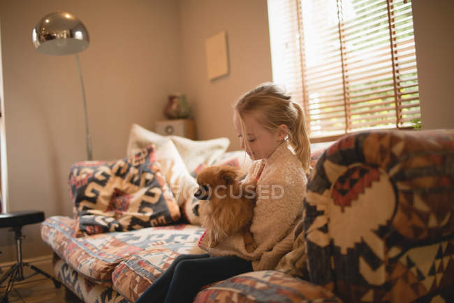 Chica con perrito sentado en el sofá en la sala de estar en casa - foto de stock
