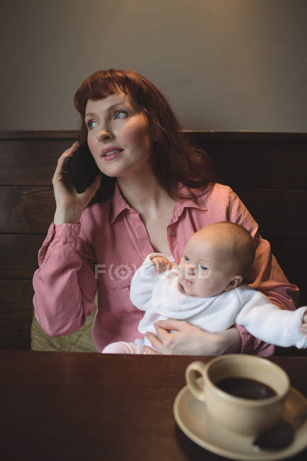 Мать с ребенком разговаривает по мобильному телефону в кафе за столом — стоковое фото
