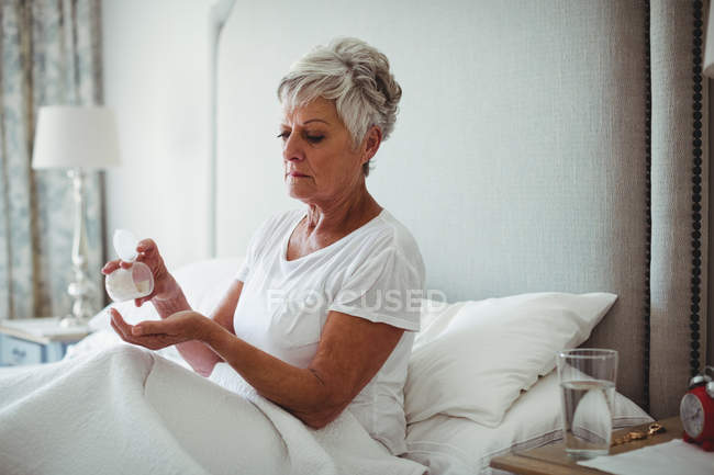 Femme âgée prenant des médicaments dans la chambre à coucher à la maison — Photo de stock