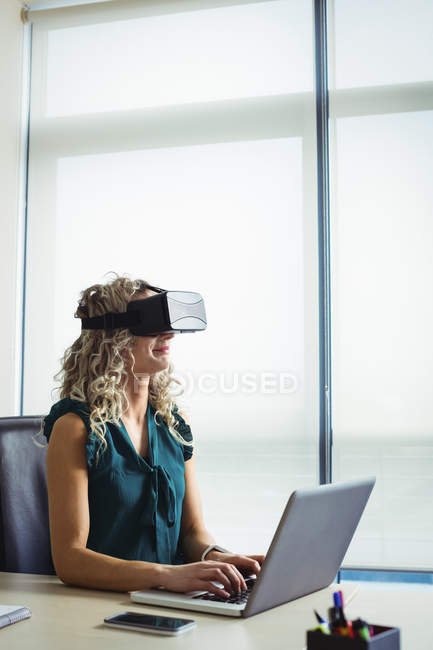 Керівник бізнесу, використовуючи гарнітуру віртуальної реальності та працюючи на ноутбуці в офісі — стокове фото