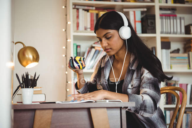 Жінка слухає музику на цифровому планшеті, маючи каву у вітальні вдома — стокове фото