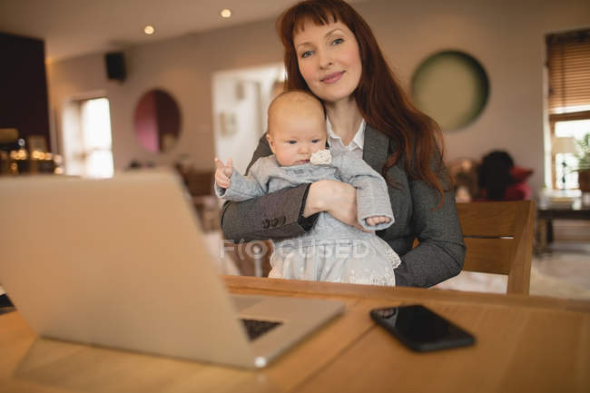 Mãe feliz sentada à mesa e segurando bebê em casa — Fotografia de Stock