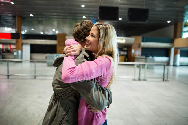 Весела пара обіймає один одного в зоні очікування в терміналі аеропорту — стокове фото