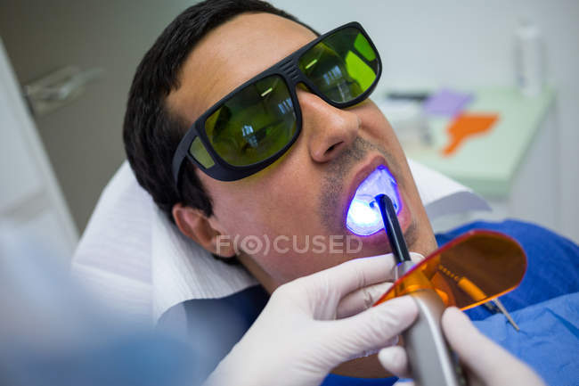 Dentiste examinant les dents des patients avec une lumière de guérison dentaire à la clinique, gros plan — Photo de stock