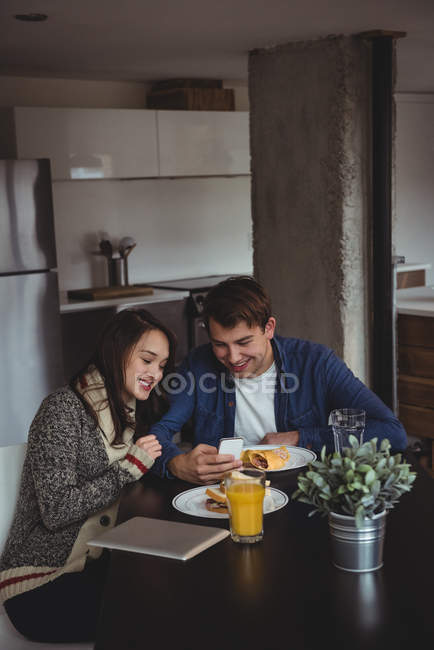 Casal usando telefone celular enquanto toma café da manhã em casa — Fotografia de Stock