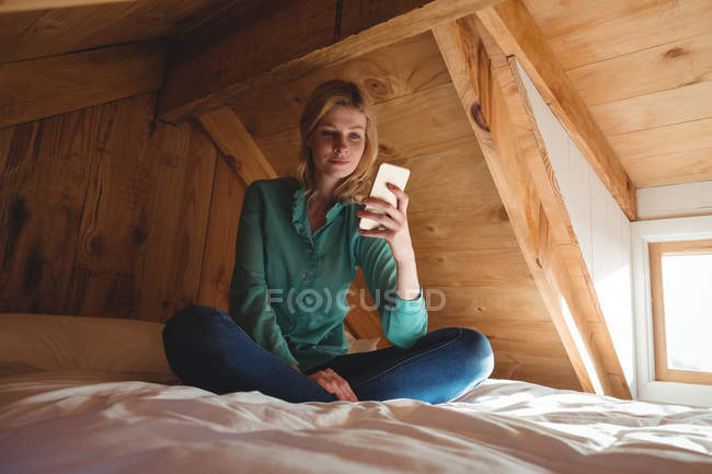 Женщина сидит на кровати и пользуется мобильным телефоном в спальне дома — стоковое фото