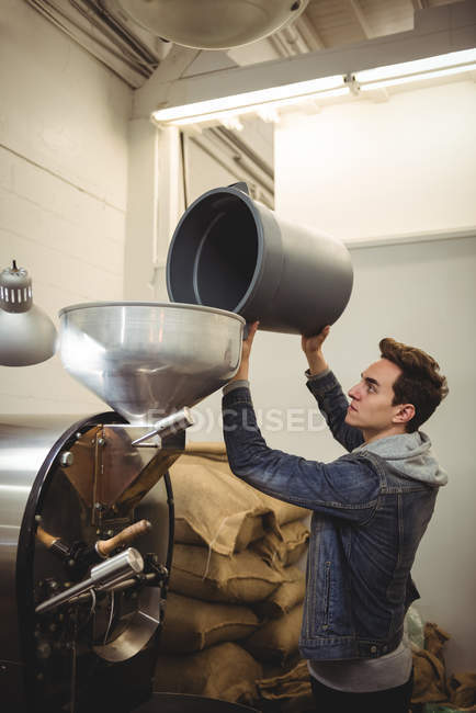 Uomo che mette i chicchi di caffè nella macchina torrefazione caffè in fabbrica — Foto stock
