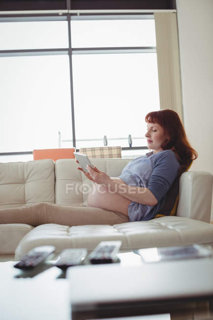 Femme enceinte tablette numérique tout en se relaxant sur le canapé dans le salon à la maison — Photo de stock