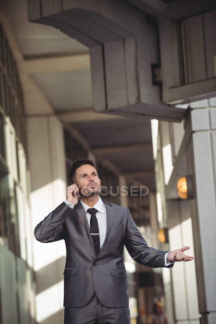 Empresário falando no celular enquanto caminha no corredor do prédio de escritórios — Fotografia de Stock