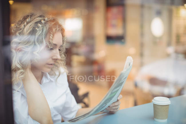 Blonde businesswoman reading newspaper at counter in cafeteria — Stock Photo
