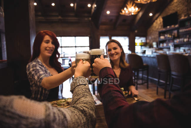 Glückliche Freunde stoßen mit Biergläsern in Bar an — Stockfoto