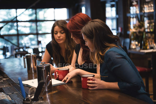 Des amis tenant des tasses à café et regardant le menu au comptoir du bar — Photo de stock