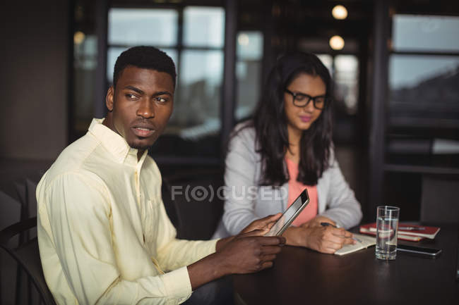 Businessman holding digital tablet while colleague writing notes in office — Stock Photo