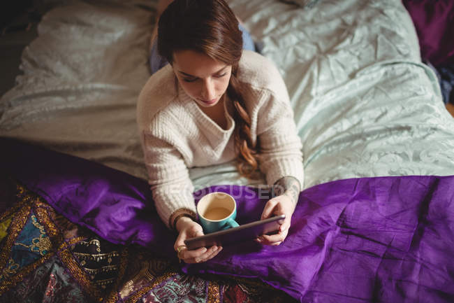 Красива жінка використовує цифровий планшет, маючи каву на ліжку вдома — стокове фото