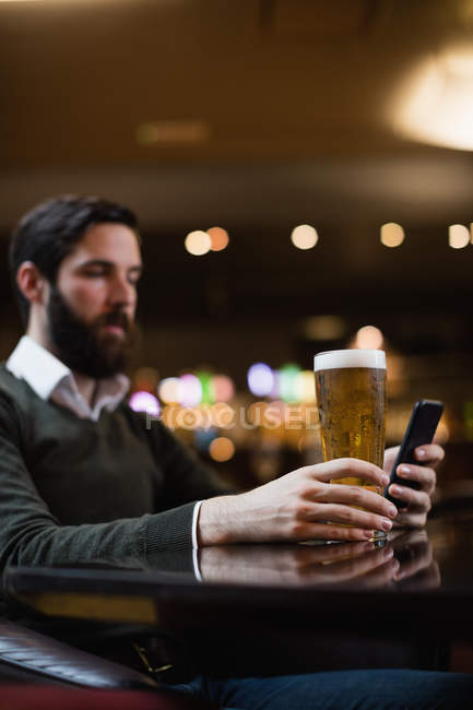 Homem olhando para o telefone celular enquanto toma um copo de cerveja no bar — Fotografia de Stock
