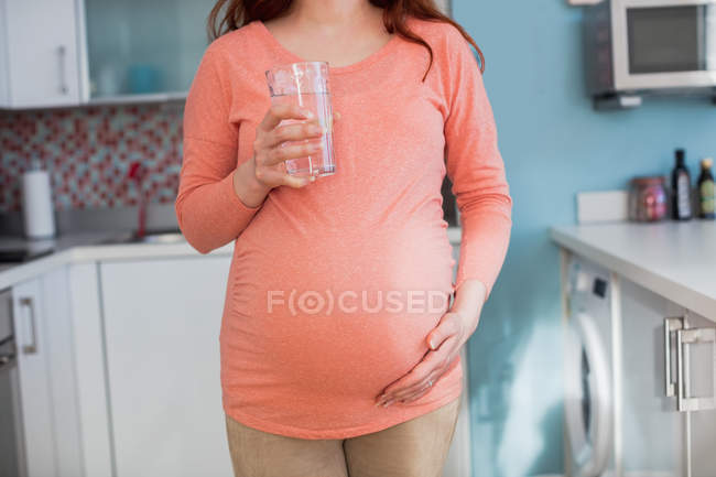 Середина вагітної жінки, що тримає склянку води на кухні вдома — стокове фото