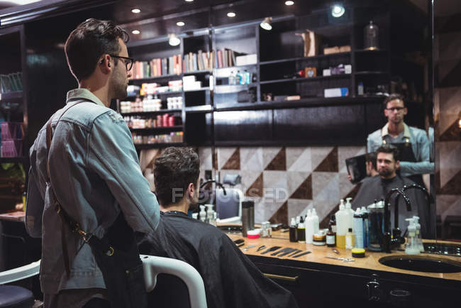 Парикмахер показывает мужчину стриженого в зеркале в парикмахерской — стоковое фото