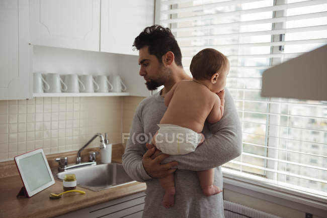 Отец смотрит на цифровой планшет, держа сына на кухне — стоковое фото