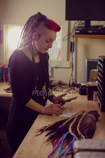 Женщина парикмахер с помощью мобильного телефона и делать заметки в магазине дредов — стоковое фото