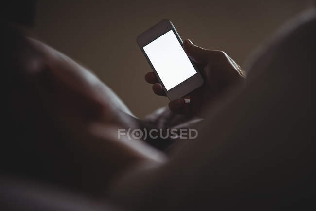Чоловік використовує свій мобільний телефон, розслабляючись в ліжку вдома — стокове фото