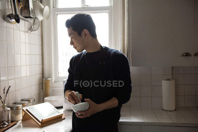 Homme utilisant pilon et mortier regardant tablette numérique à la maison — Photo de stock