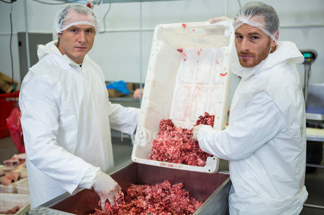 Portrait of butchers emptying minced meat in meat mincing machine at meat factory — Stock Photo