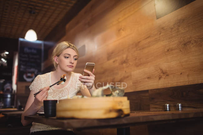 Donna che utilizza il telefono cellulare mentre mangia sushi nel ristorante — Foto stock