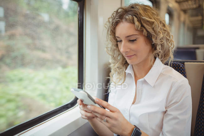 Sonriente mujer de negocios escribiendo mensaje en el teléfono inteligente mientras viaja - foto de stock