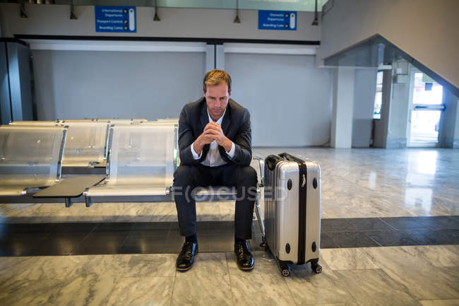 Tenso hombre de negocios sentado en la zona de espera con equipaje en la terminal del aeropuerto - foto de stock
