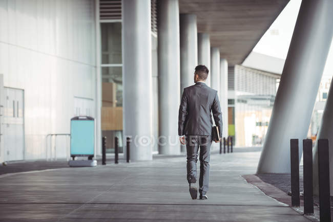 Vue arrière de l'homme d'affaires avec journal marche dans le couloir de l'immeuble de bureaux — Photo de stock