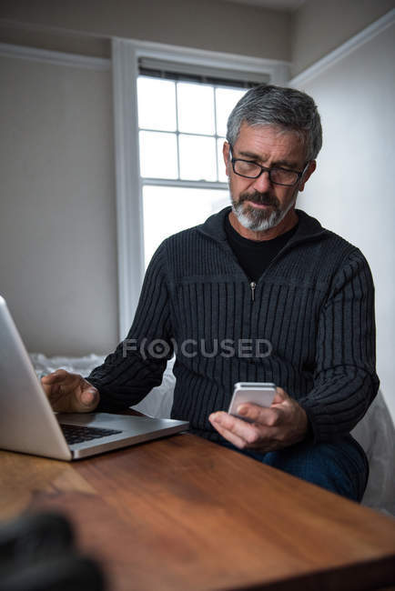 Людина використовує ноутбук і мобільний телефон у вітальні вдома — стокове фото
