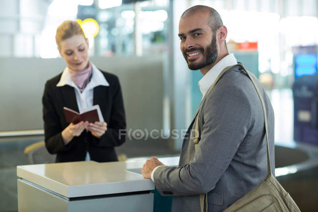 Viajeros sonrientes de pie en el mostrador mientras el asistente revisa su pasaporte en la terminal del aeropuerto - foto de stock