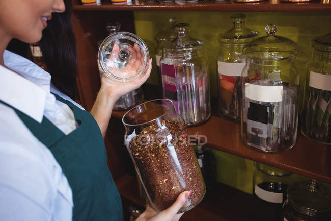 Sección media del tendero femenino sosteniendo tarro de especias en la tienda - foto de stock