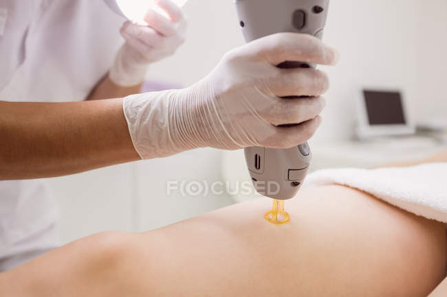 Gros plan du médecin effectuant l'épilation au laser sur la peau de la cuisse du patient en clinique — Photo de stock