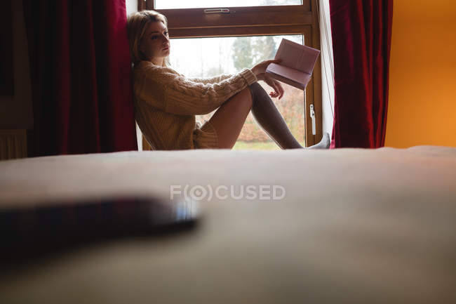 Femme assise sur la fenêtre et lisant un livre à la maison — Photo de stock