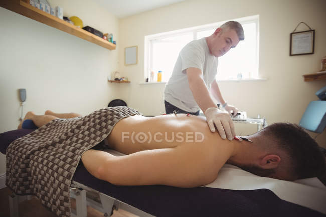 Fisioterapeuta realizando agujas electro-secas en la espalda de un paciente en la clínica - foto de stock