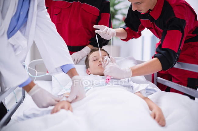 Médicos ajustando la máscara de oxígeno mientras apuran al paciente en la sala de emergencias en el hospital - foto de stock