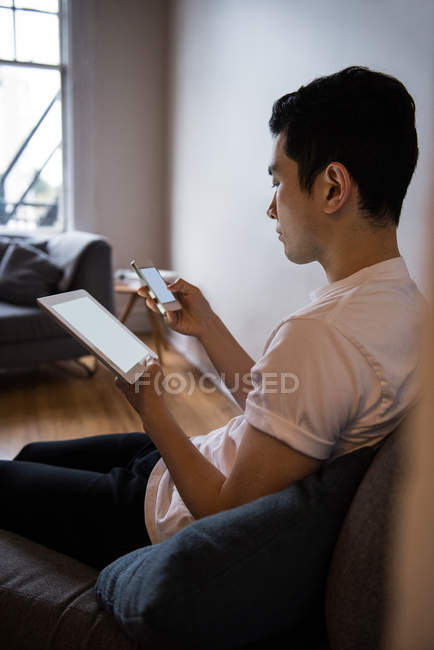 Homem usando tablet digital e telefone celular em casa — Fotografia de Stock