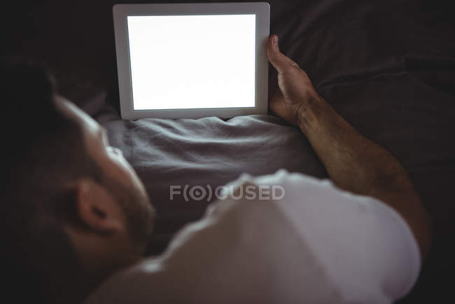 Вид сзади на человека, использующего свой цифровой планшет во время отдыха на кровати в спальне — стоковое фото