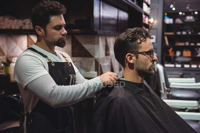 Парикмахер ставит плащ над клиентом в парикмахерской — стоковое фото