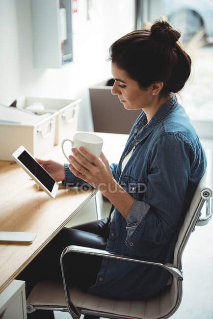Executivo de negócios usando tablet digital enquanto toma café no escritório — Fotografia de Stock
