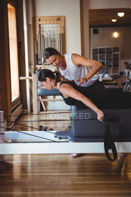 Entraîneur aidant une femme tout en pratiquant des pilates dans un studio de fitness — Photo de stock