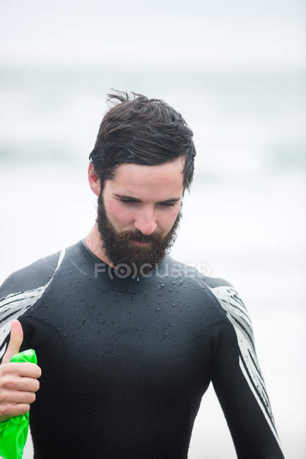 Sportler im Neoprenanzug zeigt am Strand Daumen hoch — Stockfoto
