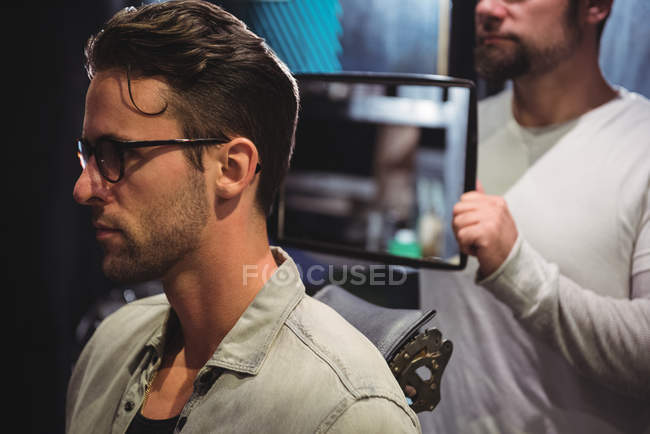 Barber showing man haircut in mirror in barber shop — Stock Photo