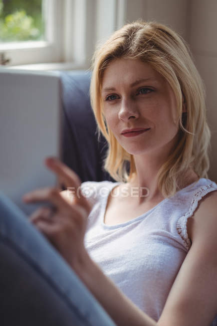 Belle femme assise sur un canapé et utilisant une tablette numérique dans le salon à la maison — Photo de stock