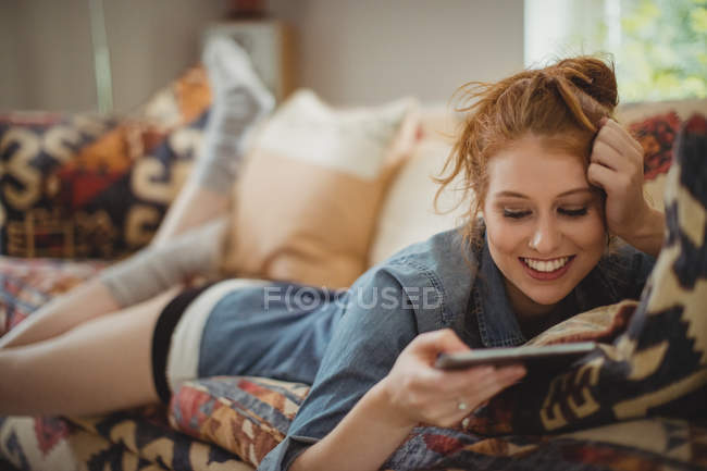 Усміхнена жінка використовує цифровий планшет, лежачи на дивані вдома — стокове фото